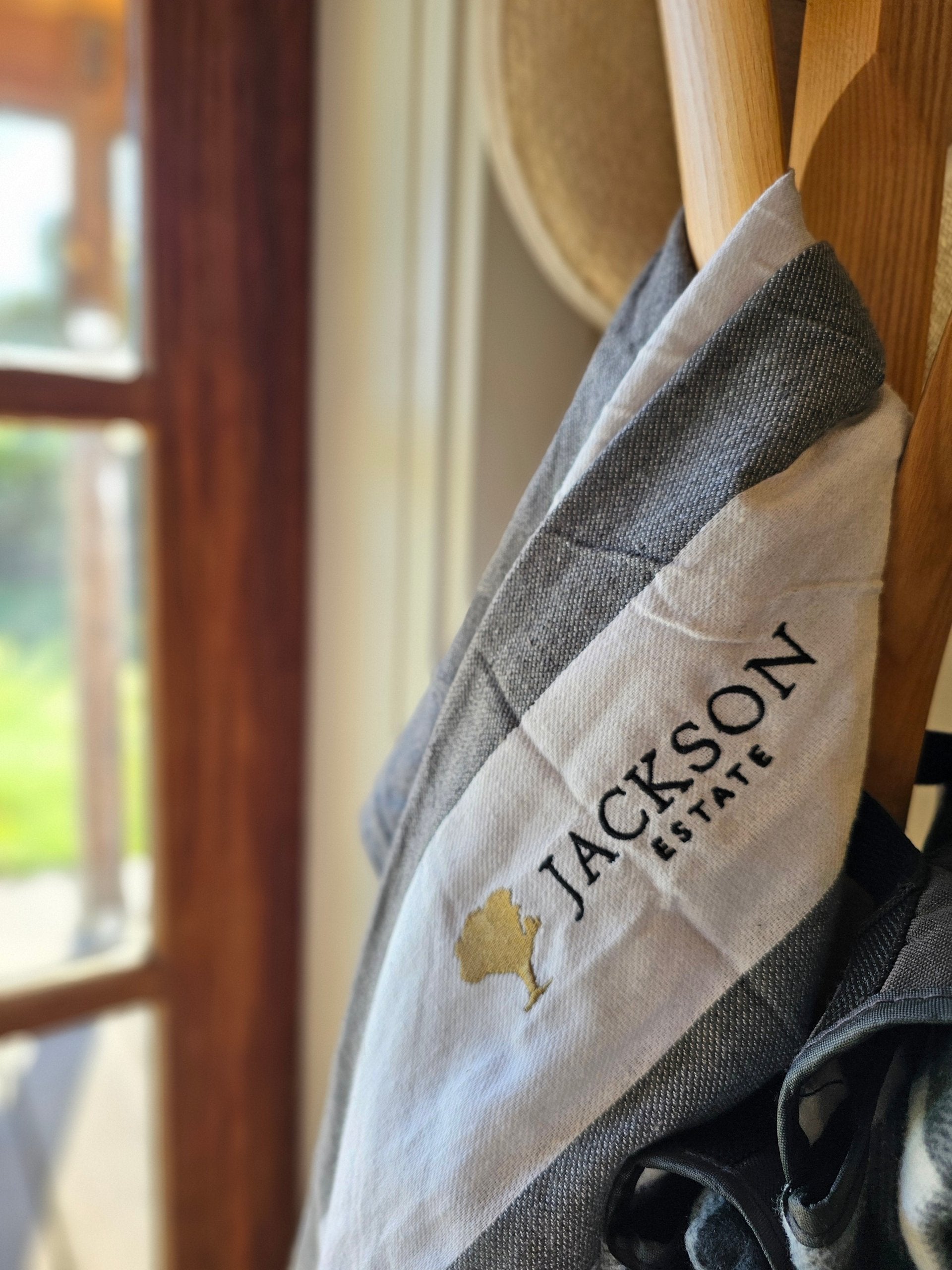 Jackson Estate branded apron hanging on a wooden hook, with a window and natural light in the background
