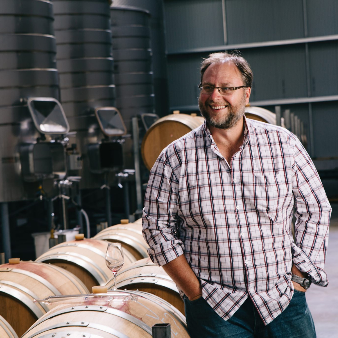 Jackson Estate winemaker smiling in the barrel hall, with oak barrels and stainless steel tanks visible behind him