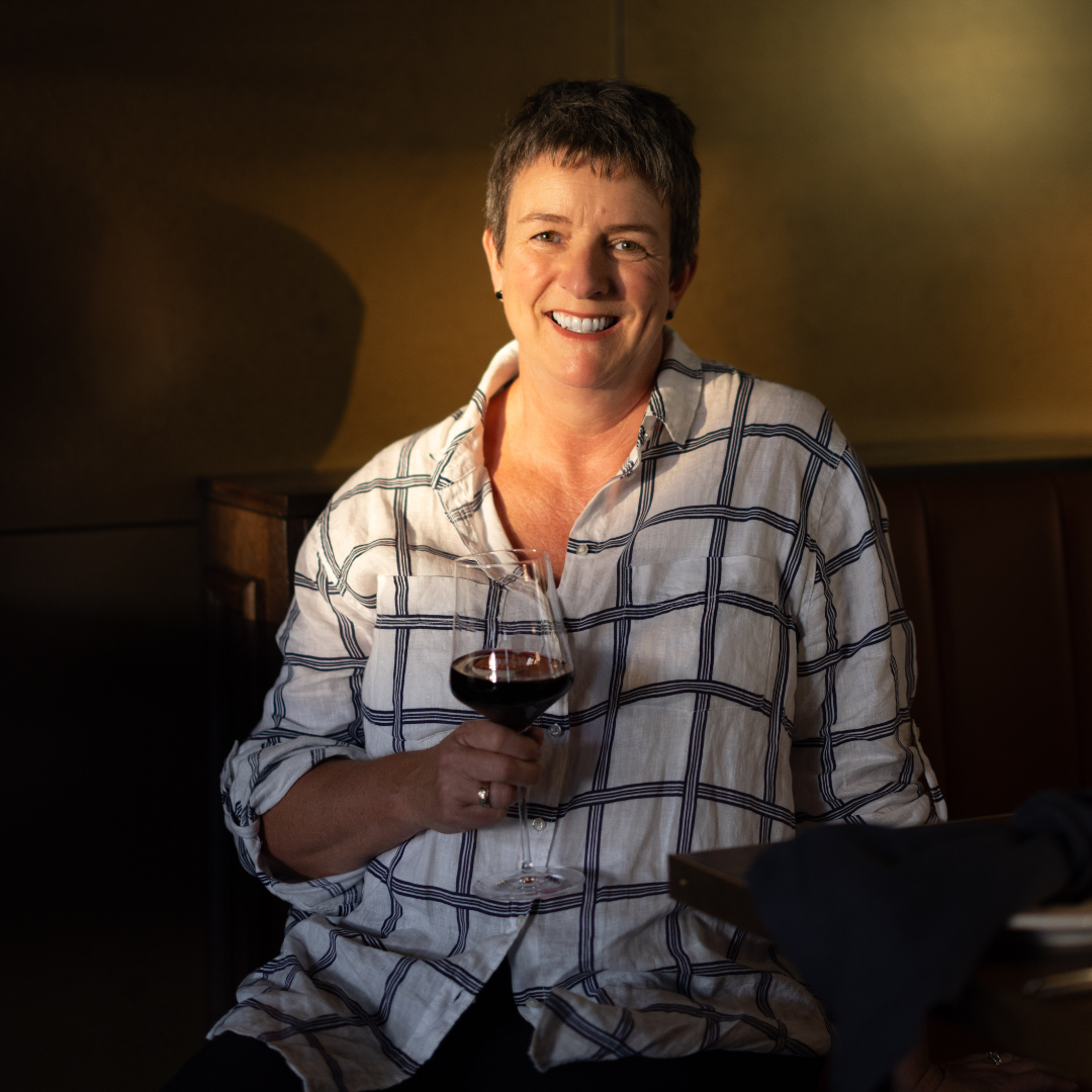 Woman smiling and holding a glass of red wine in a warmly lit interior setting