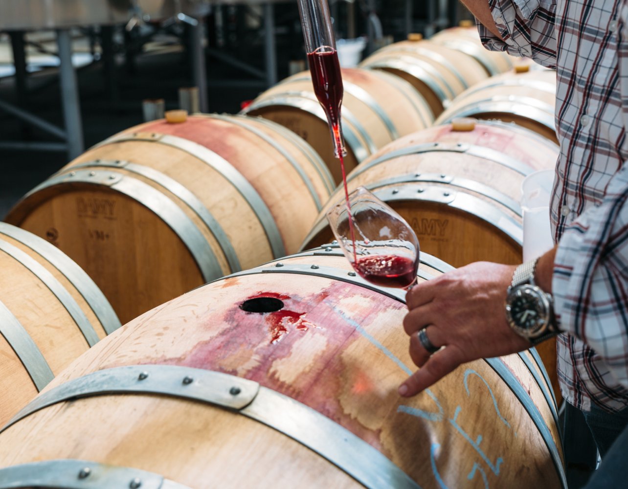 A Jackson Estate winemaker assessing a glass of red wine beside the stainless steel fermentation tanks