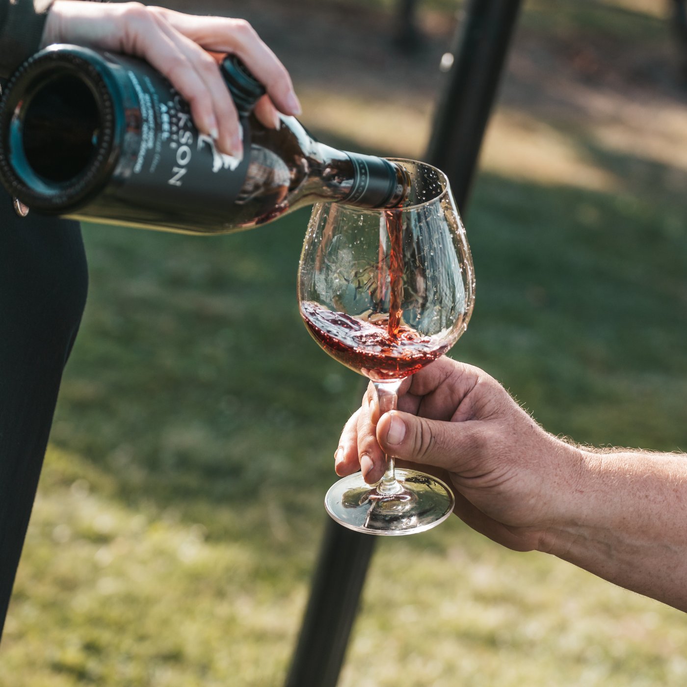 Red wine being poured from a Jackson Estate bottle into a large wine glass held outdoors in natural light.