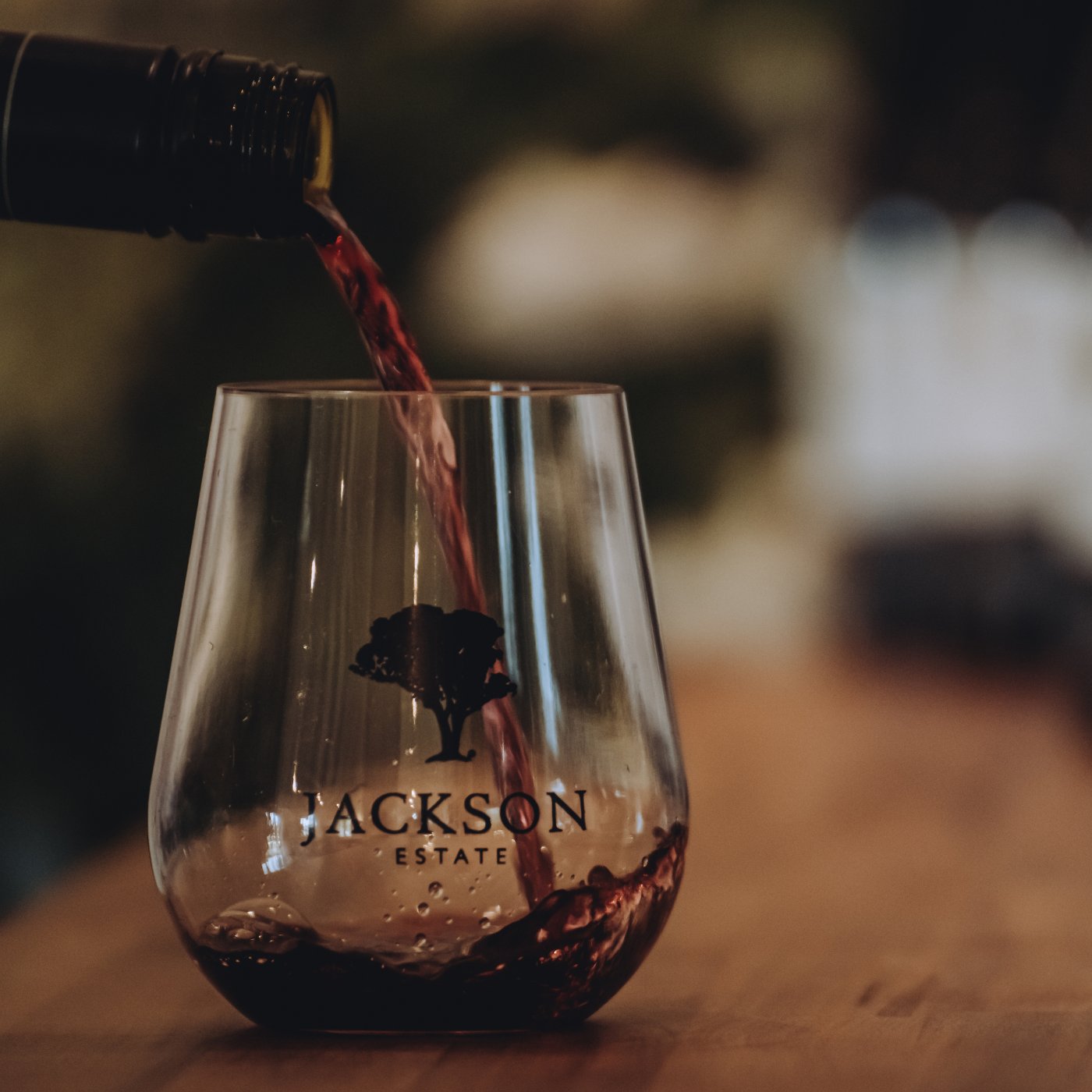 Red wine being poured into a branded Jackson Estate stemless glass on a wooden surface