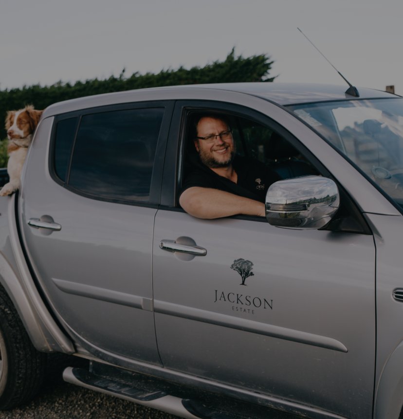 Jackson Estate winemaker Matt Patterson-Green smiling from the driver's window of a branded ute, dog on the back cab