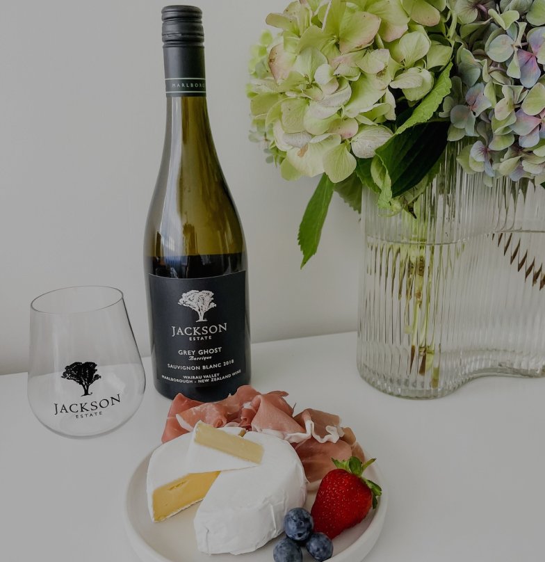 Jackson Estate Grey Ghost Sauvignon Blanc bottle with a branded glass, cheese and charcuterie plate, and hydrangeas in a vase