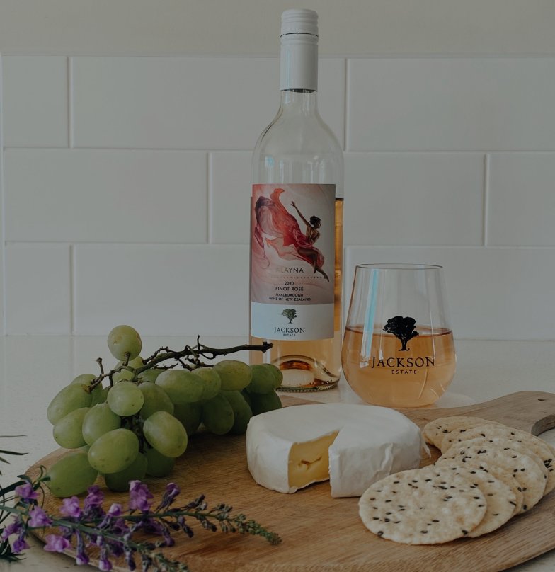 Jackson Estate Rayna Pinot Rosé bottle and branded glass with grapes, brie, and crackers on a wooden board