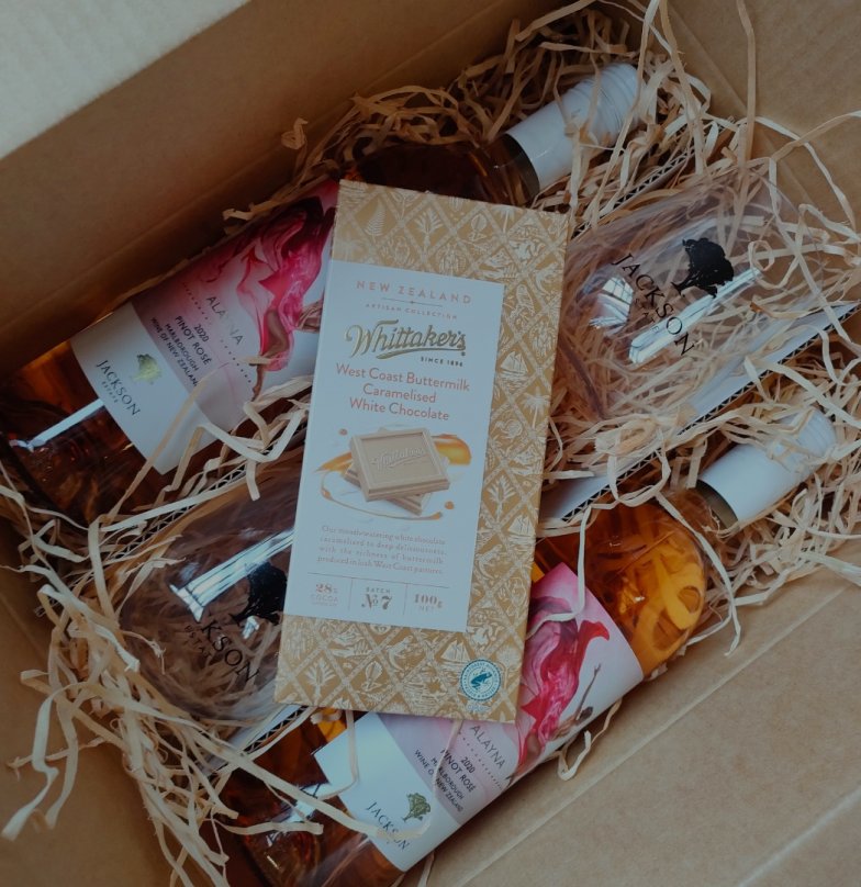 Gift box filled with Jackson Estate wine bottles and a Whittaker's West Coast Buttermilk Caramelised White Chocolate bar, nestled in straw packaging