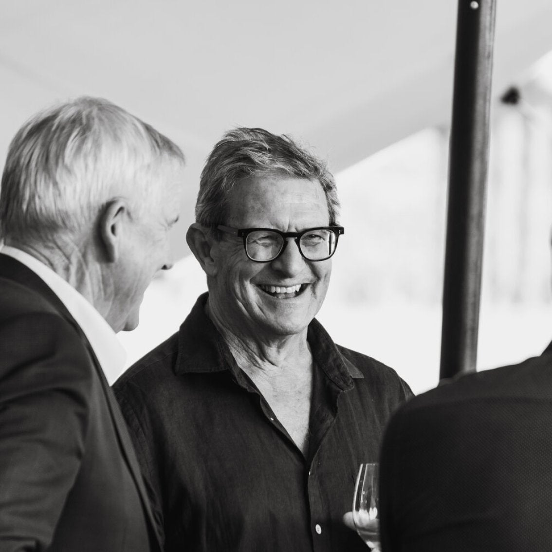 Two men laughing together at an outdoor event, one holding a wine glass, black and white photo