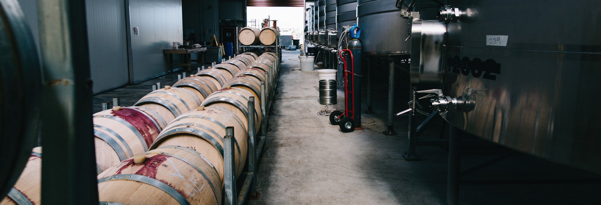 Row of oak wine barrels alongside large stainless steel tanks inside the Jackson Estate winery