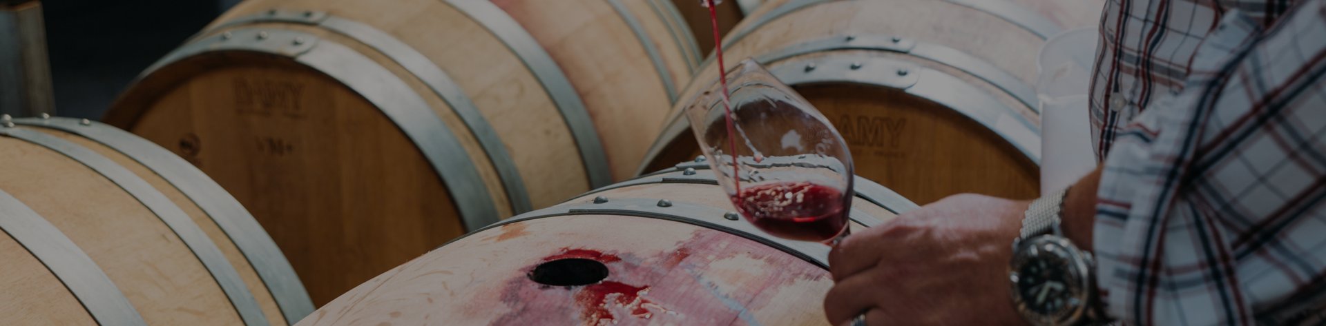 Red wine being poured into a glass beside oak barrels at Jackson Estate winery