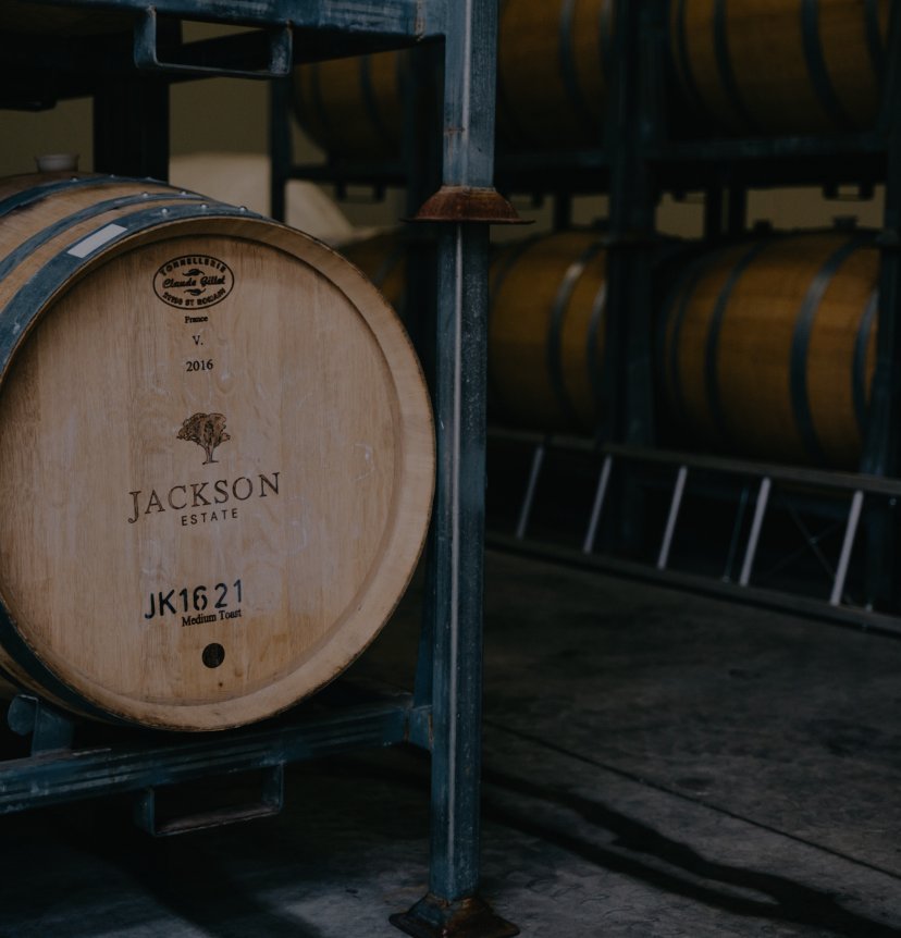 Jackson Estate branded oak wine barrel in a dimly lit barrel room, with rows of barrels visible in the background